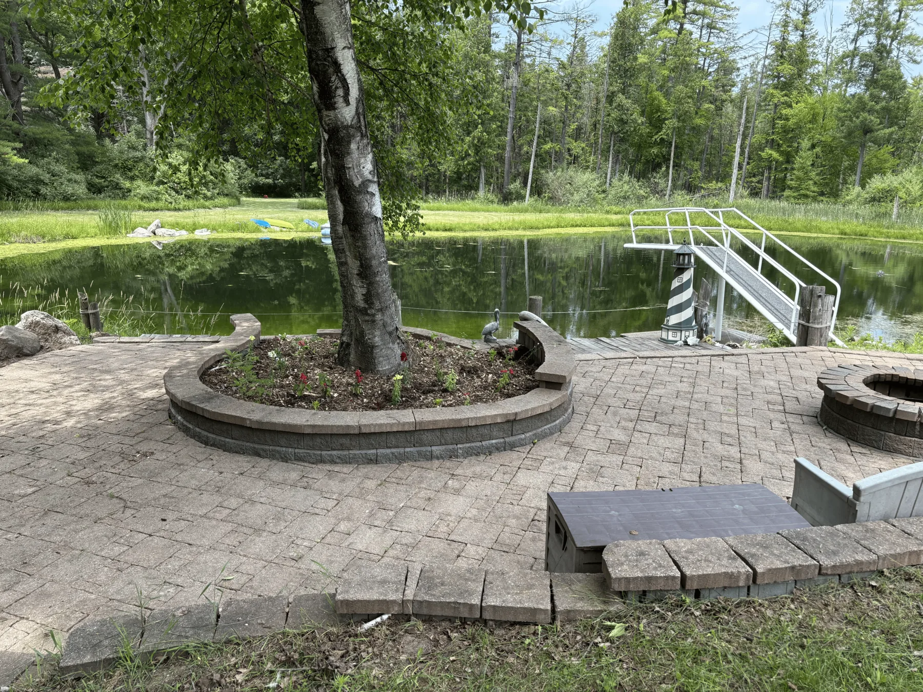 Landscaped patio with firepit, mature shade tree and pond beyond