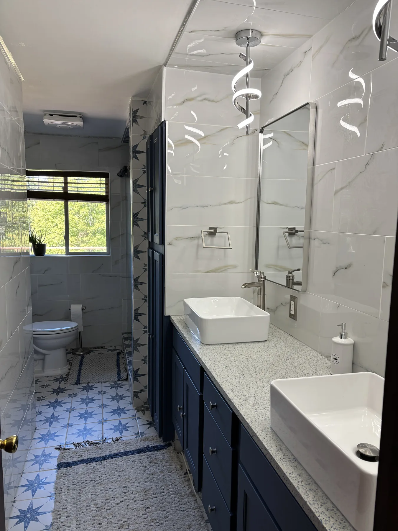 Remodeled primary bathroom with dual sinks, quartz countertop, illuminated mirror and tiled shower