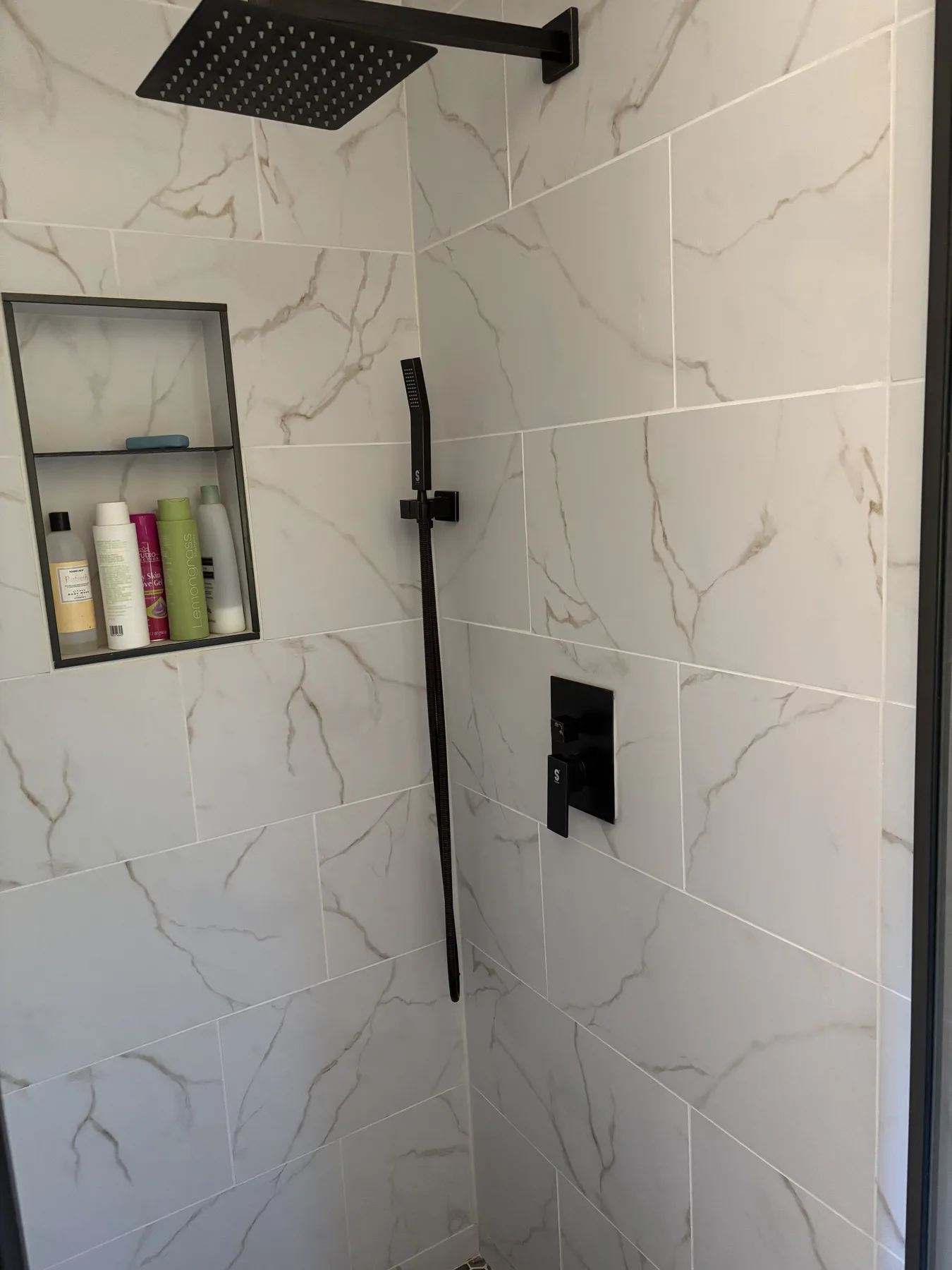 Bright marble-look tiled shower with black fixtures and recessed shelf
